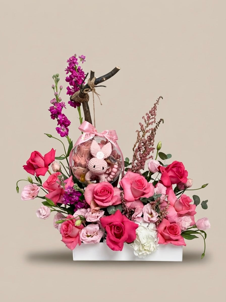 Pink rose and stock flower box arrangement with a hanging acrylic keepsake bubble enclosing a pink crochet animal, styled by Plaza Hollandi at Ezdan Mall.   