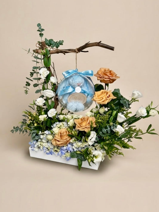 Baby Bloom Bubble newborn boy flower arrangement featuring champagne roses, blue hydrangeas, and an acrylic keepsake bubble with a blue plush toy.   