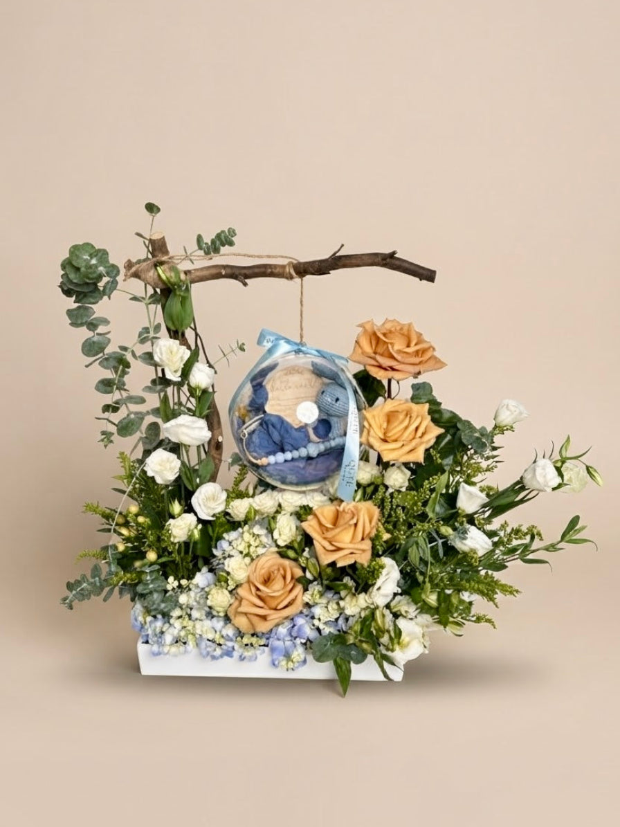 Baby Bloom Bubble newborn boy flower arrangement featuring champagne roses, blue hydrangeas, and an acrylic keepsake bubble with a blue crochet bunny, Hello World card, and custom name clip.