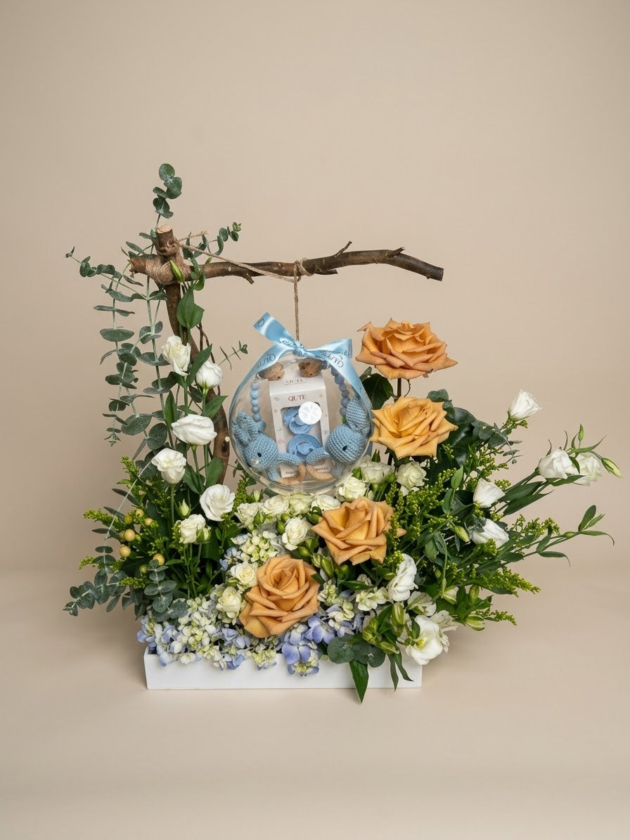 Baby Bloom Bubble twin baby boys flower arrangement featuring champagne roses, blue hydrangeas, and an acrylic keepsake bubble with two crochet rattles, personalized clips, and custom bibs.