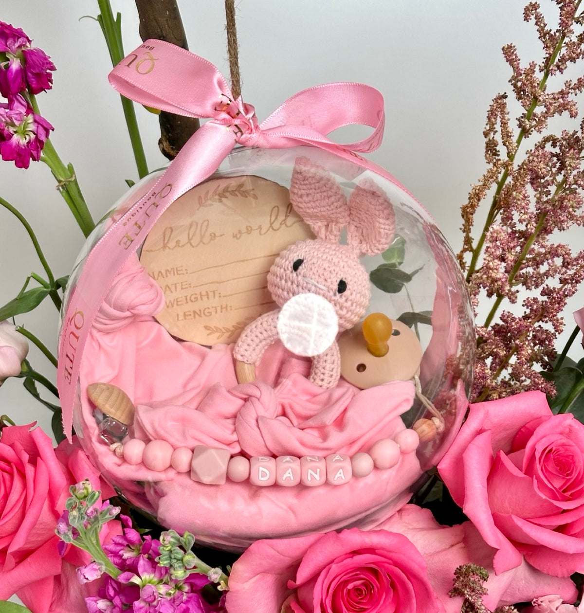 Lush white floral box filled with vibrant pink roses and purple stock, featuring a clear bubble holding a custom jersey swaddle, matching accessories, a pacifier, and a bunny toy.   
