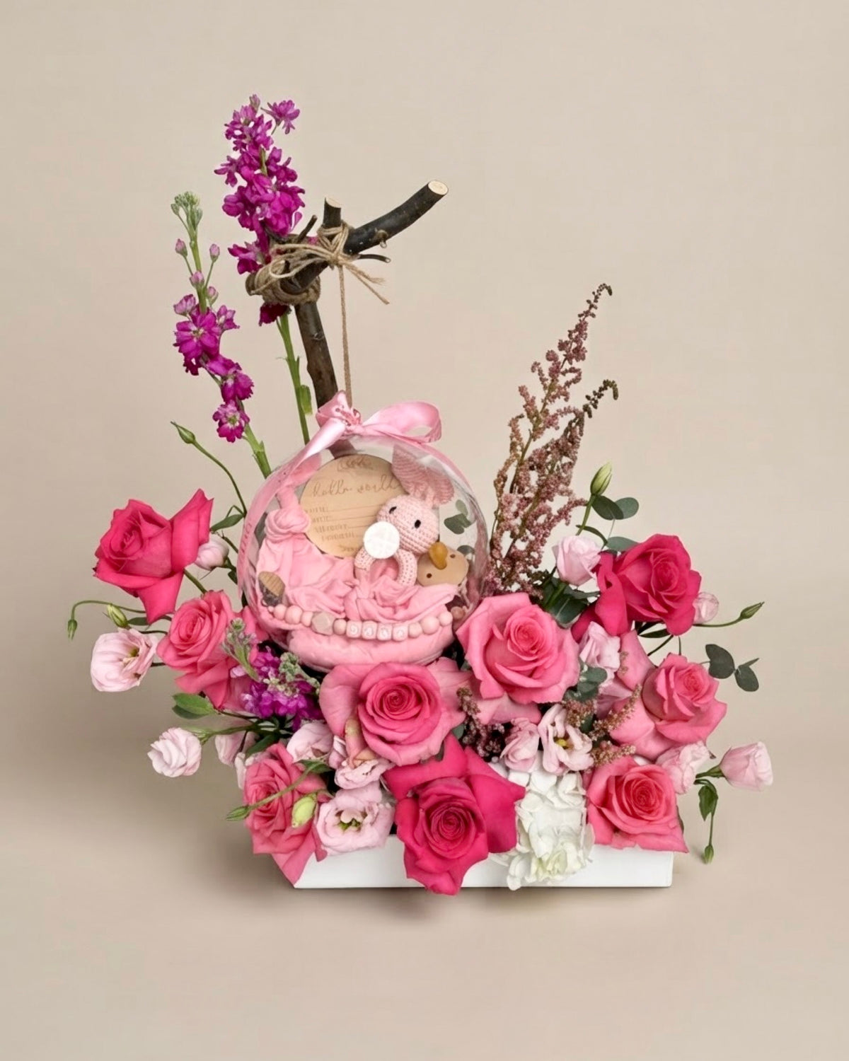Lush white floral box filled with vibrant pink roses and purple stock, featuring a clear bubble holding a custom jersey swaddle, matching accessories, a pacifier, and a bunny toy.   
